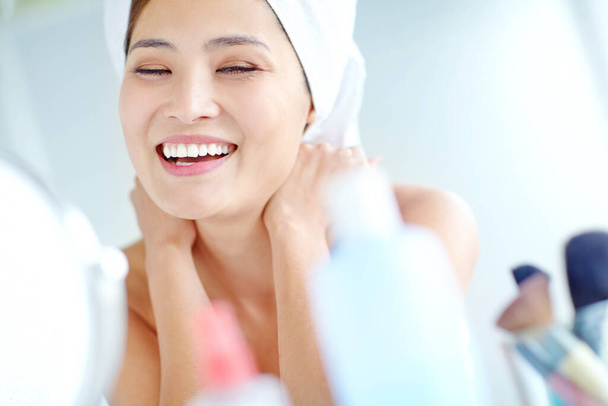 Довольна своей красотой. Красивая молодая азиатка улыбается, сидя в ванной с полотенцем на голове - Фото, изображение
