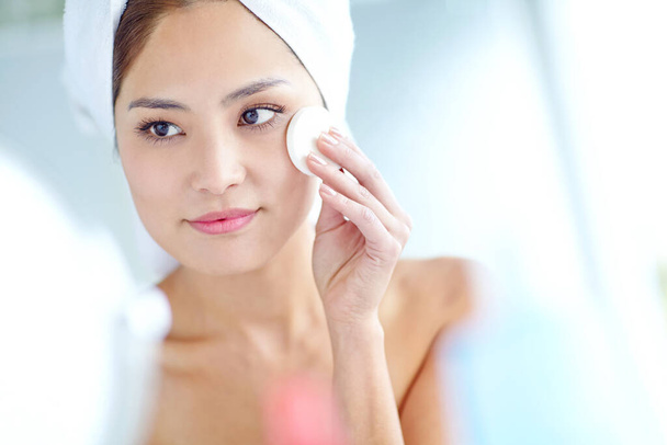 Natural skincare. An attactive young Asian woman applying moisturizer with a towel on her head - Foto, Imagem