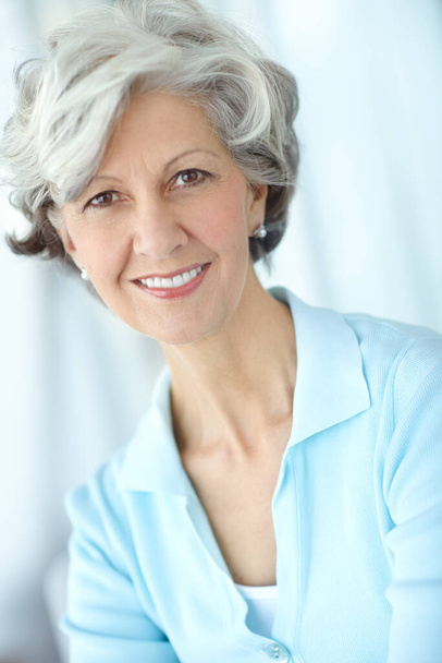 Portrait of one happy senior caucasian woman with grey hair enjoying free time at home. Face of carefree, wise and cheerful retired lady smiling, feeling optimistic about life and ageing gracefully. - 写真・画像