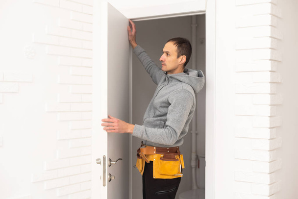Young handyman installing a white door in a room. - Foto, afbeelding
