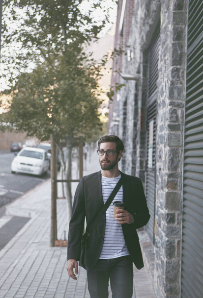 Raakte de stad trottoirs met een koffie in de hand. een jonge man die onderweg een kopje koffie drinkt terwijl hij in de stad loopt - Foto, afbeelding