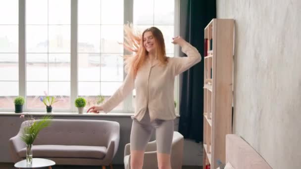 Moving shot female renter homeowner silly funky Caucasian woman in pajamas jump on bed happy free carefree girl having fun jumping dancing to music in bedroom home hotel weekend celebrating at morning - Footage, Video