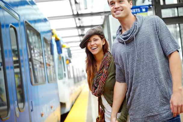 Το ταξίδι μας φέρνει πιο κοντά. Ένα γελαστό ζευγάρι κρατιέται χέρι-χέρι σε ένα σταθμό τρένου περιμένοντας ένα τρένο. - Φωτογραφία, εικόνα