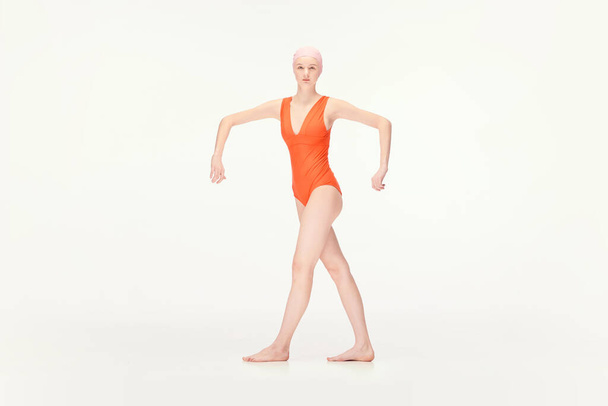 Young girl in red swimsuit and swimming cap standing in position with broad hands isolated over white background. Concept of retro style, sport, fashion, youth, vintage. Copy space for ad - Φωτογραφία, εικόνα