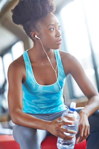 Shes going to reach her goals. a beautiful young woman listening to music and taking a water break at the gym - Foto, imagen