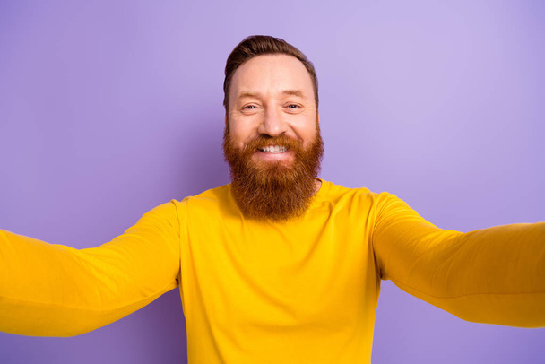 Selfie retrato de joven blogger chico pelo rojo barba mantenga cámara grabando su nuevo video dientes blancos aislados en color violeta fondo. - Foto, imagen