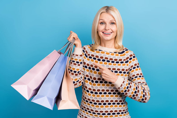 Portrait of excited charming lady indicate finger hand hold mall shopping bags isolated on blue color background. - Foto, imagen