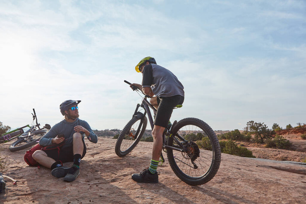 Na drodze do chwały. Pełne ujęcie dwóch atletycznych mężczyzn robiących sobie przerwę podczas jazdy na rowerze górskim po pustyni - Zdjęcie, obraz