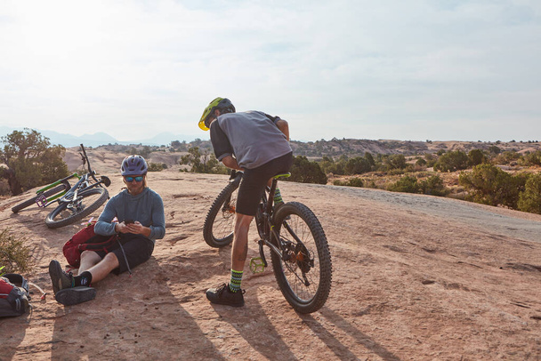Entusiastas de ciclismo em seu elemento. Tiro de comprimento total de dois homens atléticos fazendo uma pausa enquanto mountain bike pelo deserto - Foto, Imagem