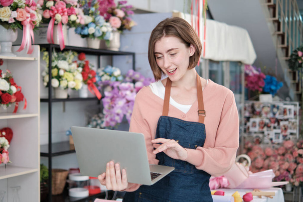 Portrait of one young White female florist owner in apron with laptop in bright and beautiful flower shop store smiles with online shopping jobs, small e-commerce business, happy SME entrepreneur.  - Valokuva, kuva