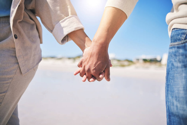 Se tenant la main, l'amour et un couple marchant sur la plage pour la romance, le soutien ou un rendez-vous. Contenu, vacances et un homme et une femme avec affection sur une promenade à l'océan pour l'engagement et la confiance ensemble. - Photo, image