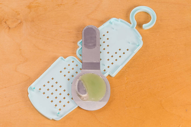 Moth lék v podobě gelu v kapsli leží na jeho otevřené plastové speciální kontejner s hákem pro zavěšení mezi uložené oblečení - Fotografie, Obrázek