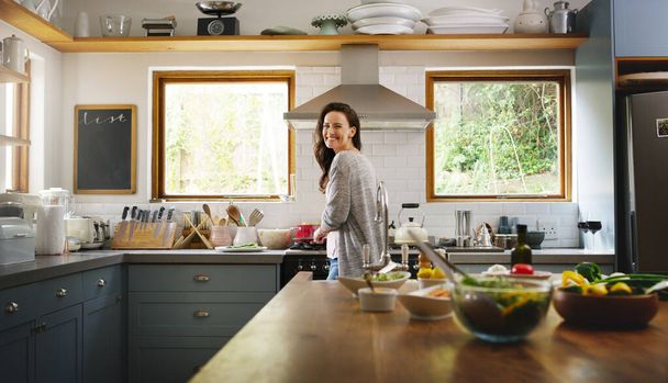 Портрет привлекательной молодой женщины, улыбающейся во время приготовления пищи на кухне дома - Фото, изображение