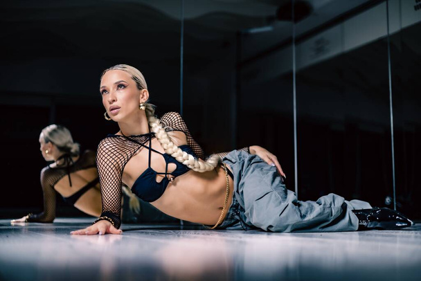 A beautiful female dancer in a mesh overlay crop top in black and baggy pants posing on the floor - Foto, Imagem