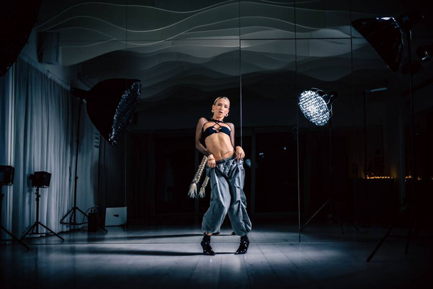 A beautiful female dancer posing in mesh overlay crop top in black and baggy pants in a studio - Foto, imagen