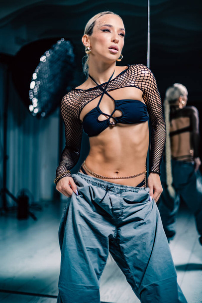 A vertical shot of a beautiful female dancer posing in mesh overlay crop top in black and baggy pants - Zdjęcie, obraz