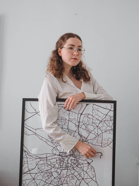 A vertical shot of a woman posing with a framed artwork on the background of a white wall - Fotografie, Obrázek