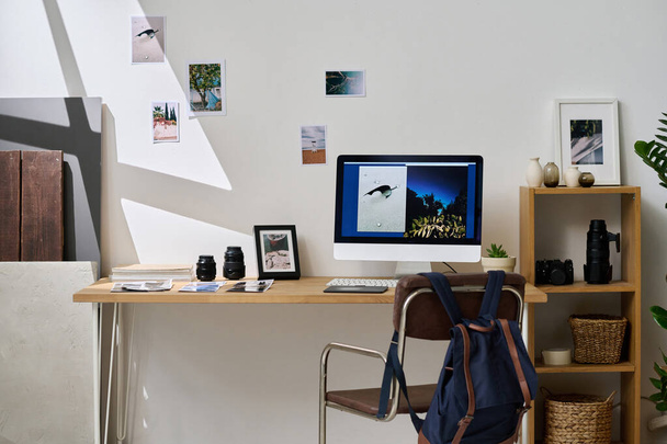 Immagine orizzontale di posto di lavoro moderno di designer grafico con computer e fotografie professionali su parete in studio - Foto, immagini