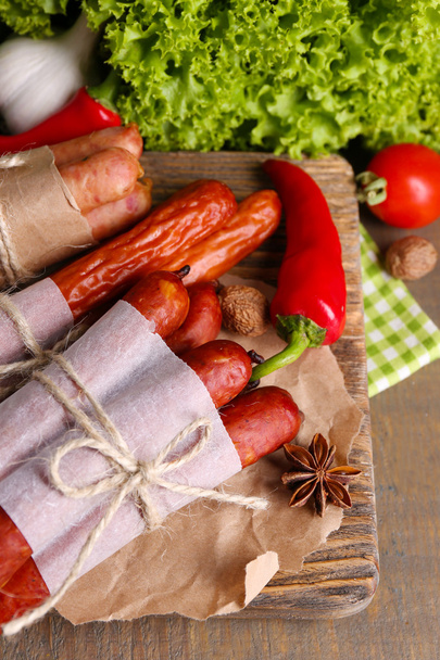 Assortment of thin sausages, mustard in bowl and spices on cutting board, on wooden background - Фото, зображення