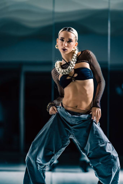 A vertical shot of a beautiful female dancer posing in mesh overlay crop top in black and baggy pants - Foto, imagen