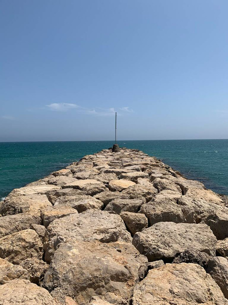 A vertical shot of a rocky jetty against the background of the teal sea and blue sky. - Фото, изображение