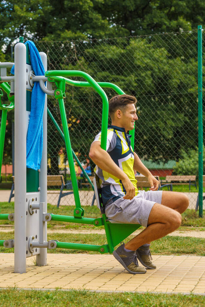 Young handsome man working out in outdoor gym. Sporty guy flexing his muscles on machine. Staying fit and healthy. - Foto, afbeelding