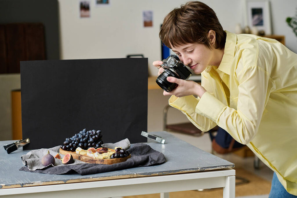 Jovem fotógrafa tirando fotos de frutas frescas em bandeja de madeira com câmera durante seu trabalho em estúdio - Foto, Imagem