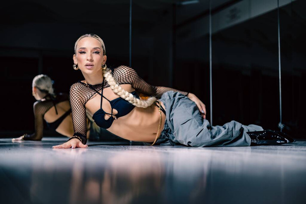 A beautiful female dancer in a mesh overlay crop top in black and baggy pants posing on the floor - Foto, imagen