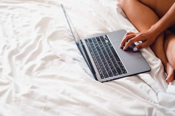 Кавказка лежит на кровати с ноутбуком, ноутбук на пустой кровати - Фото, изображение
