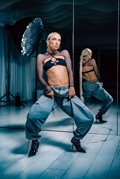 A vertical shot of a beautiful female dancer posing in mesh overlay crop top in black and baggy pants - Фото, изображение