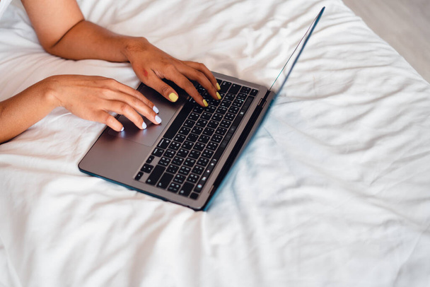 Donna caucasica sdraiata sul letto utilizzando il computer portatile, computer portatile sul letto vuoto - Foto, immagini