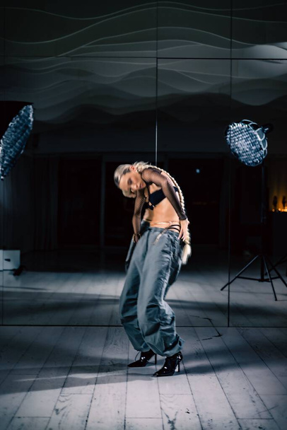 A sexy blonde with long braid ponytail posing in studio with mirrors on the walls in stylish outfit - Foto, Bild