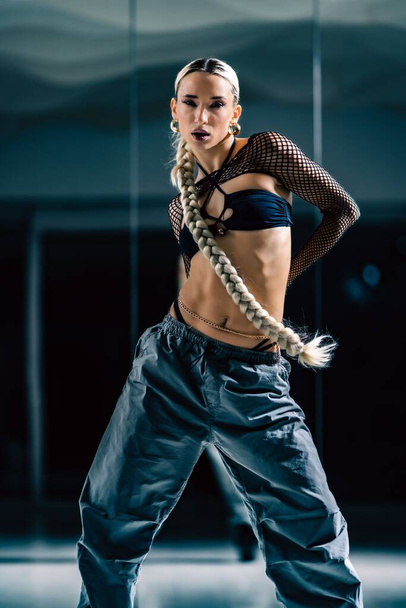 A vertical shot of a beautiful female dancer posing in mesh overlay crop top in black and baggy pants - Zdjęcie, obraz