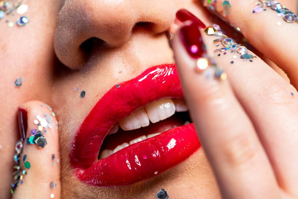 Close-up of beautiful young woman with bright red glossy lipstick touching face with shiny glitters - Fotó, kép