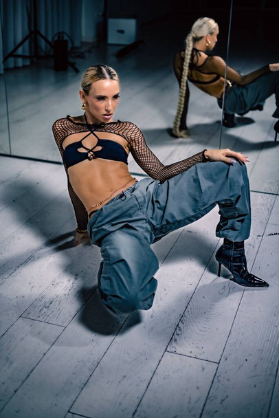 A beautiful female dancer in a mesh overlay crop top in black and baggy pants posing on the floor - Fotó, kép