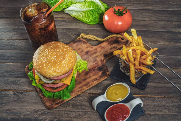hamburger complete with two meats, sauces, french fries and cola on an antique wooden board. - Zdjęcie, obraz