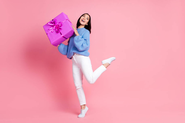 Photo of pleasant grateful woman straight hairdo dressed knit pullover hold gift look empty space isolated on pink color background. - Fotó, kép