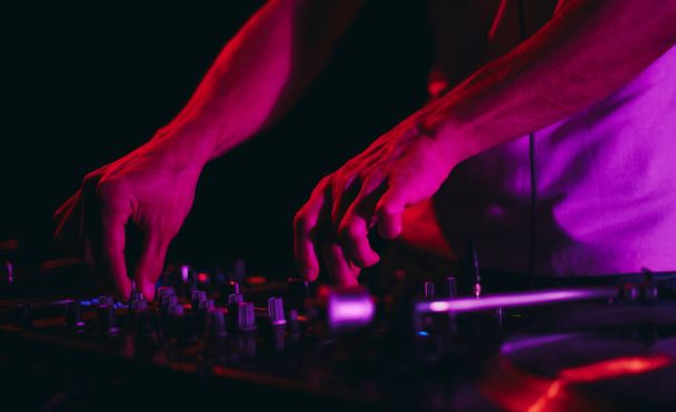Hands of a disc jockey mixing music with a sound mixer device. Disc jockey playing techno set in a dark night club - Photo, image