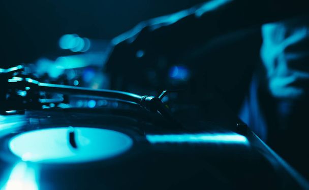 Dj turntable playing vinyl record with music in dark night club. Disc jockey performing on a techno festival  - Foto, Imagen