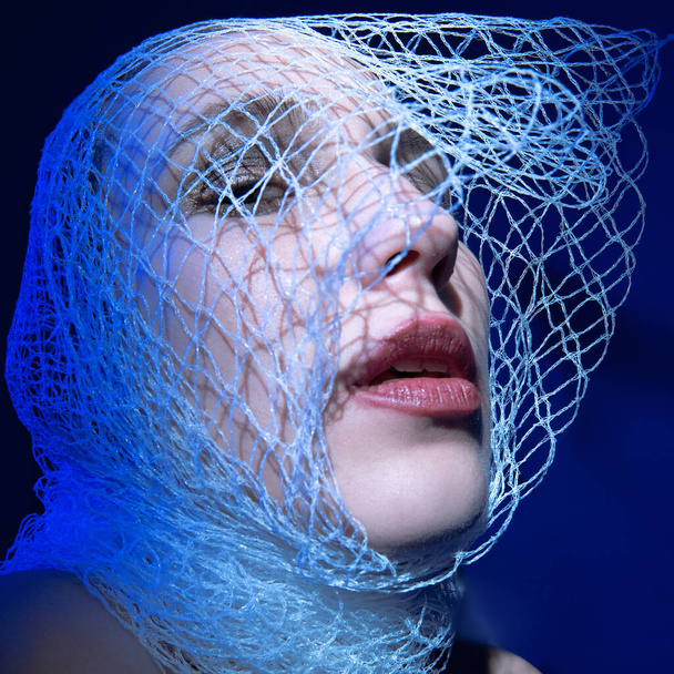 a girl wrapped in a net in the blue light hides her face in the  - Foto, Imagem
