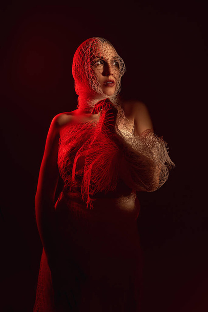 a girl wrapped in a net in the red light hides her face in the s - Fotografie, Obrázek