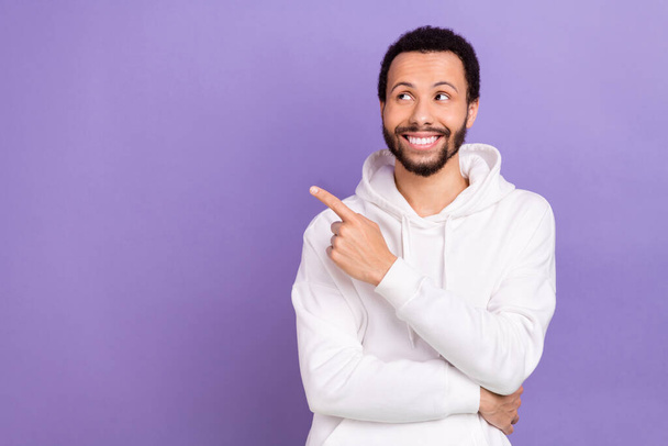 Portrait of cheerful handsome guy brunet beard white pullover indicating look at sale empty space isolated on violet color background. - Photo, Image