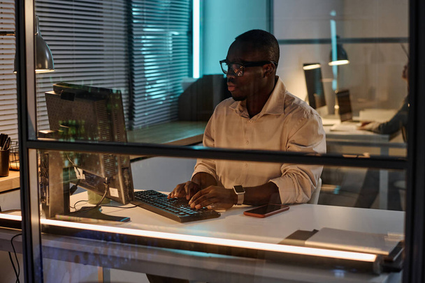 Afroamerykanin biznesmen koncentrujący się na pracy na komputerze podczas pracy w ciemnym biurze - Zdjęcie, obraz