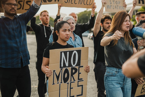 Группа многонациональных протестующих в повседневной одежде с картонными плакатами, стоящими на улице и кричащими громкоговорителю во время беспорядков - Фото, изображение