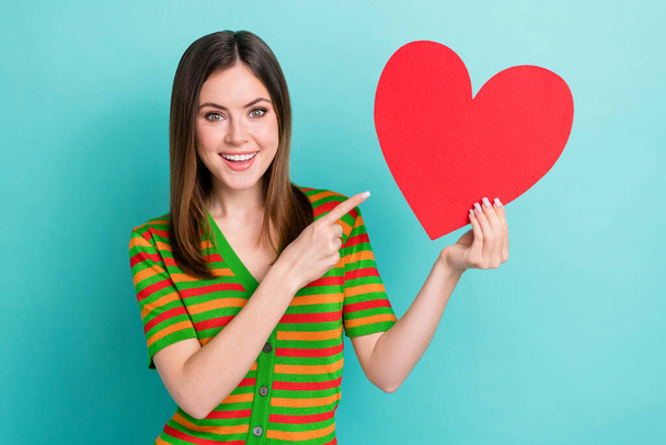 Photo of cheerful shiny woman dressed striped cardigan pointing finger big red heart isolated teal color background. - Фото, изображение