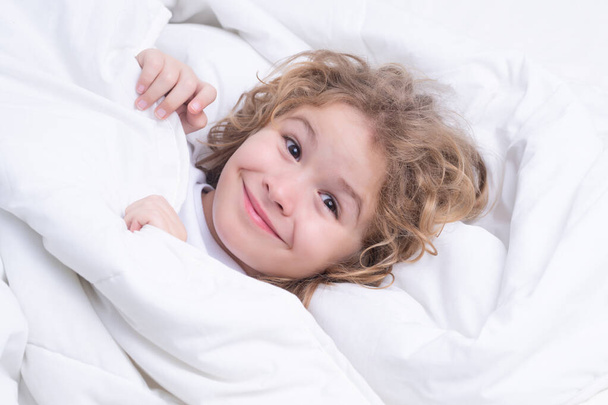 Child enjoys sunny morning. Good time at home. Kid wakes up from sleep. Child wakes up in morning in bed. Morning awakening little child in bed - Foto, afbeelding