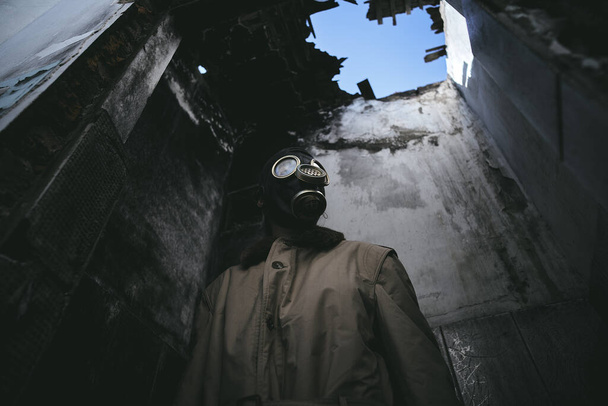 Mies, jolla on kaasunaamari raunioituneessa rakennuksessa, vuotava katto pimeässä, maailmanloppu, hyvä kirjan kanteen, matala kulma - Valokuva, kuva