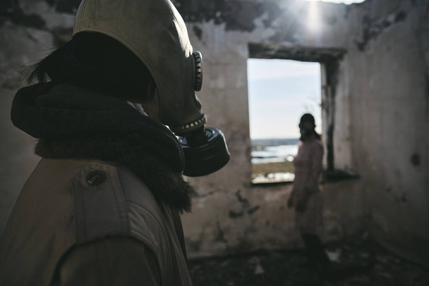 Two people, a guy and a girl in gas masks, stand inside an abandoned house  and look at each other, apocalypse - Photo, image