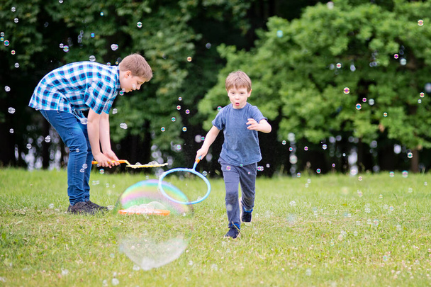 夏休みだ。学校だ。公園では二人の兄弟がシャボン玉で遊んでいる。ピクニックをしている陽気な幸せな家族。自然の中で町の休暇や旅行. - 写真・画像