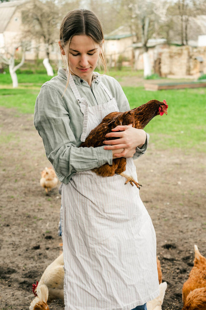an attractive young woman holding a hen in her hands and smiling at the camera - Foto, imagen